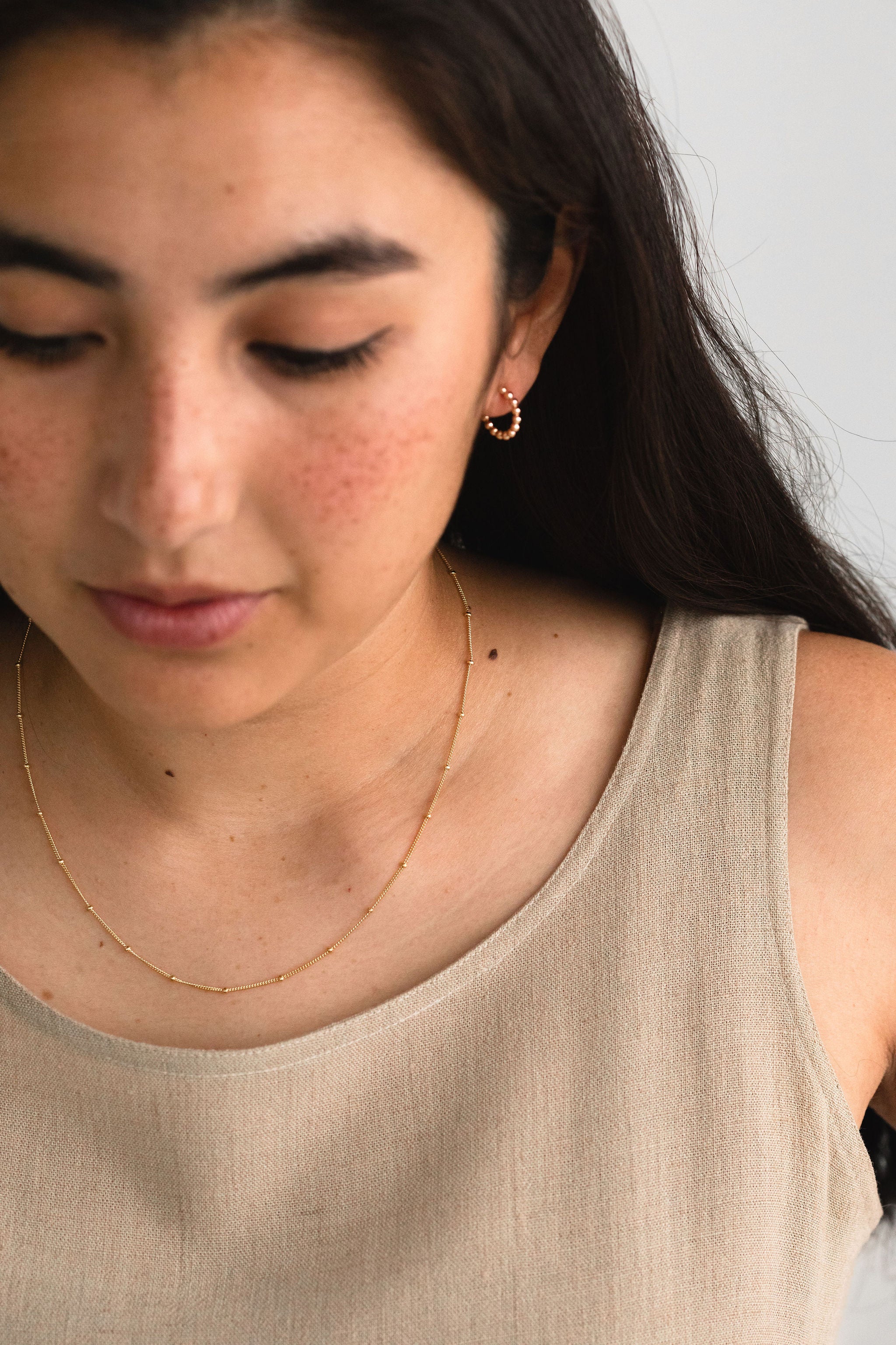 Minimalist gold filled earrings with plan background wearing dot hoop earrings and delicate satellite necklace