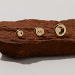Three handcrafted 14k gold Molten Pebble studs with unique organic texture displayed on red clay stone, showing small, medium, and large size options of sculptural earrings