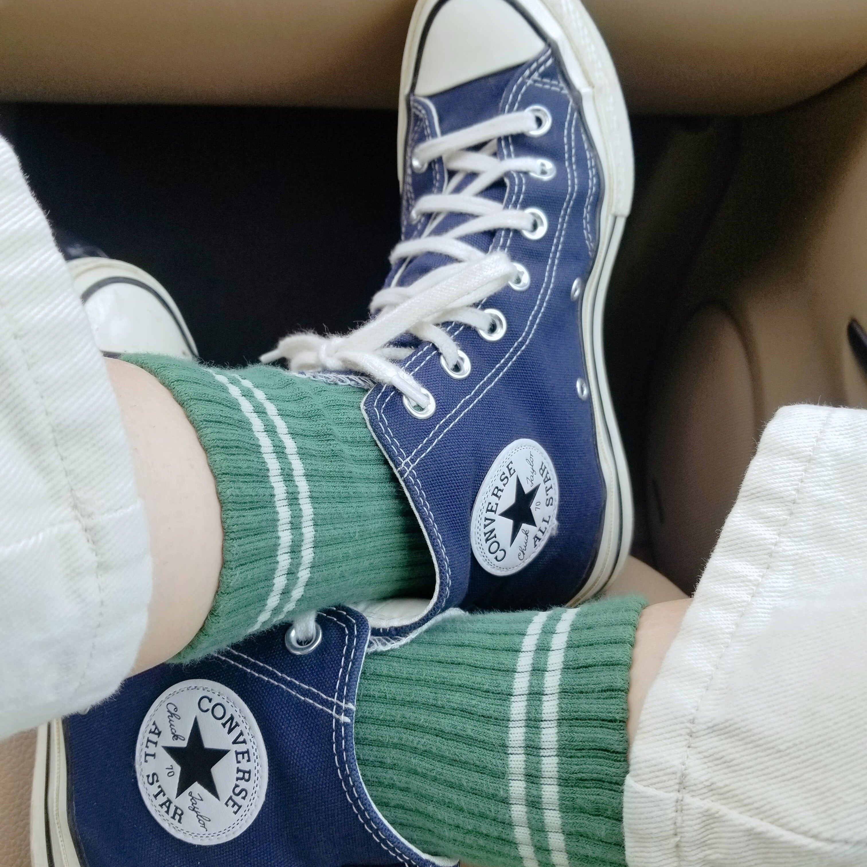 Blue Converse sneakers with white laces and green socks worn by a person.