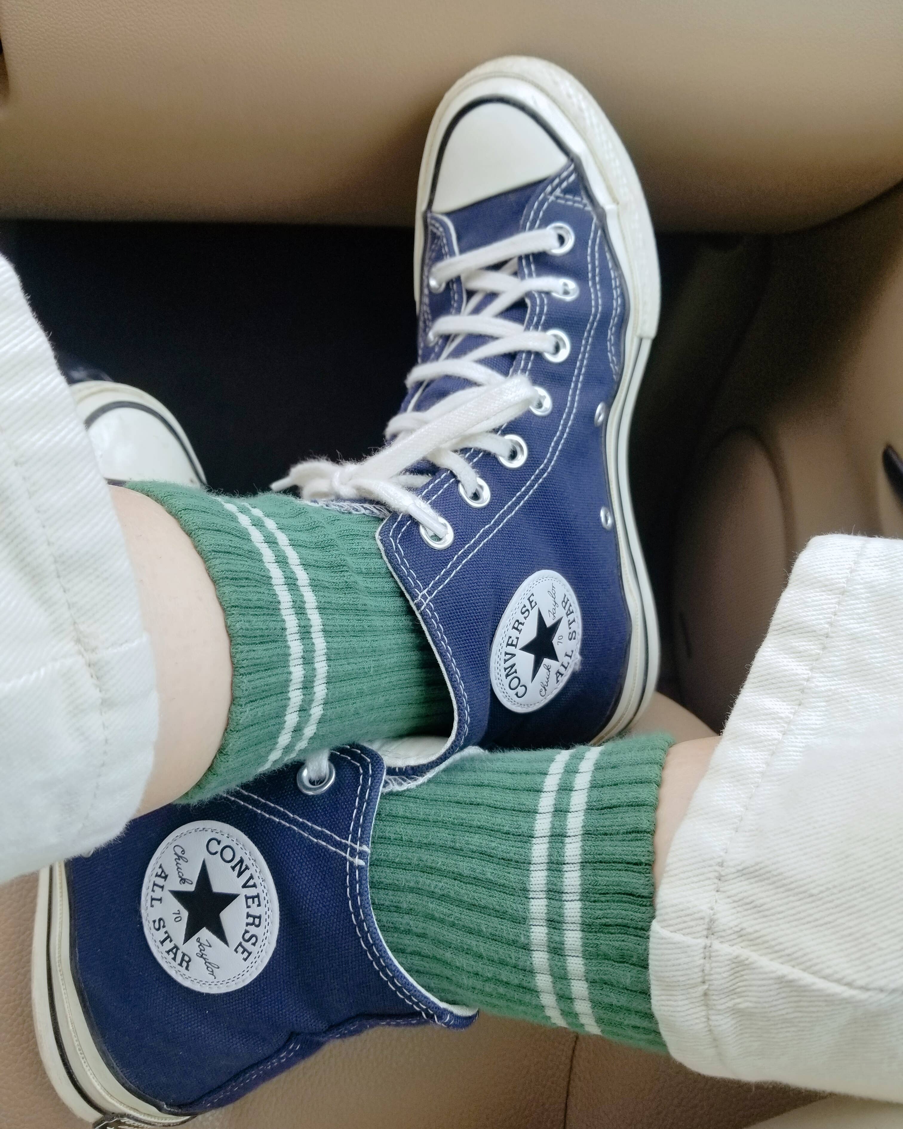 Blue Converse sneakers with white laces and green socks worn by a person.