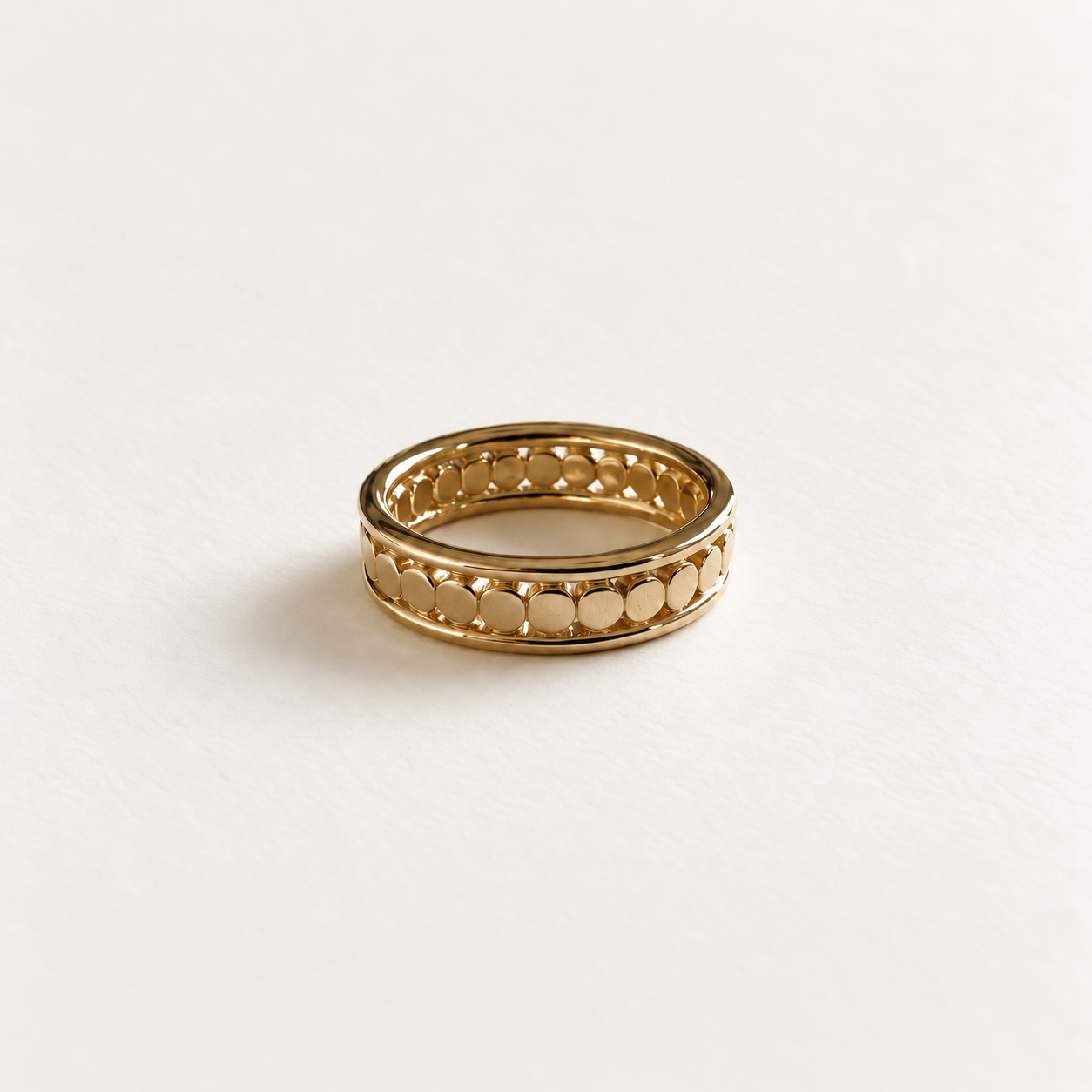 A gold band ring with a textured, openwork pattern of small circular and diamond-like shapes, photographed on a clean, light off-white background.