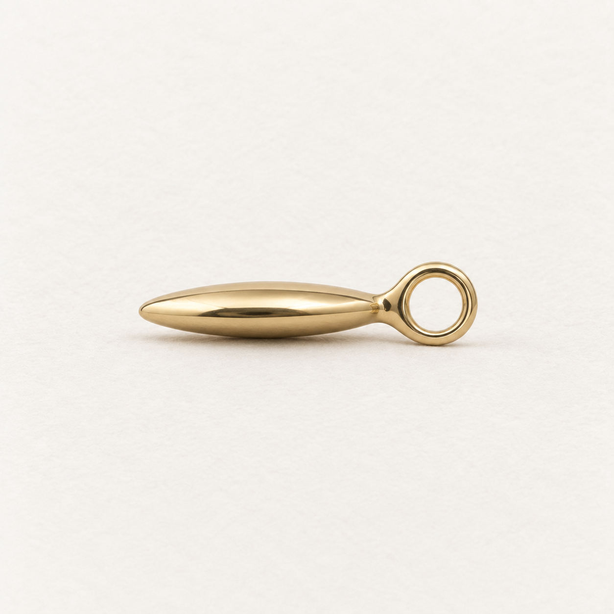 A polished gold metal pendant necklace with a teardrop-shaped key blade, shown on a clean, light off-white background.
