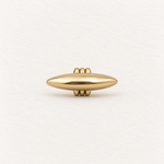 A polished gold capsule-shaped pendant with three small rings at the bail at the top and bottom, centered on a textured off-white background.
