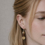 Close-up of a woman wearing gold earrings with a neutral background