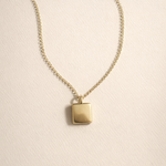 Gold necklace with a square pendant on a beige background