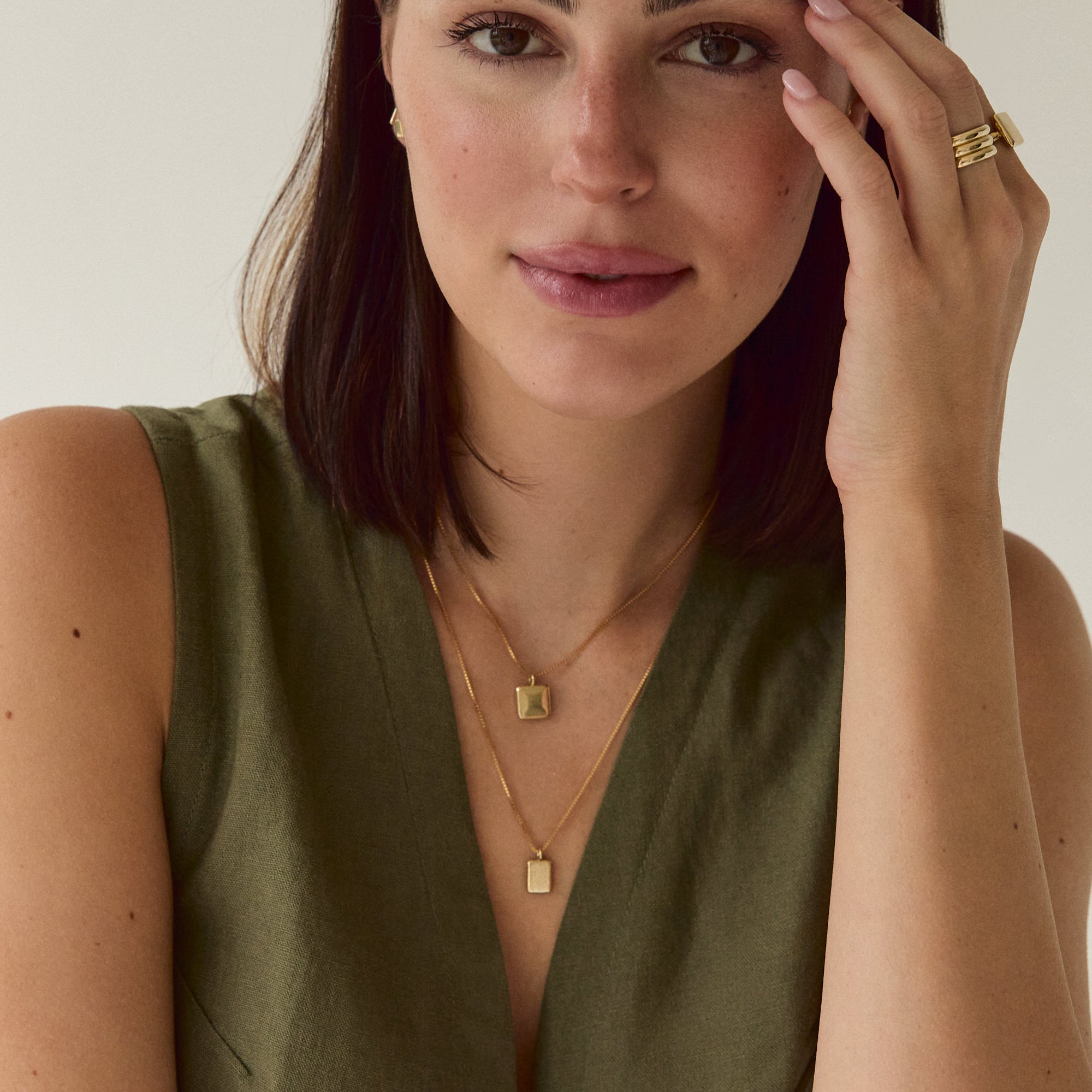 A delicate gold box chain necklace with a small rectangular gold pendant on model