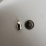 A small polished silver teardrop pendant with a reflective finish, shown next to a dime