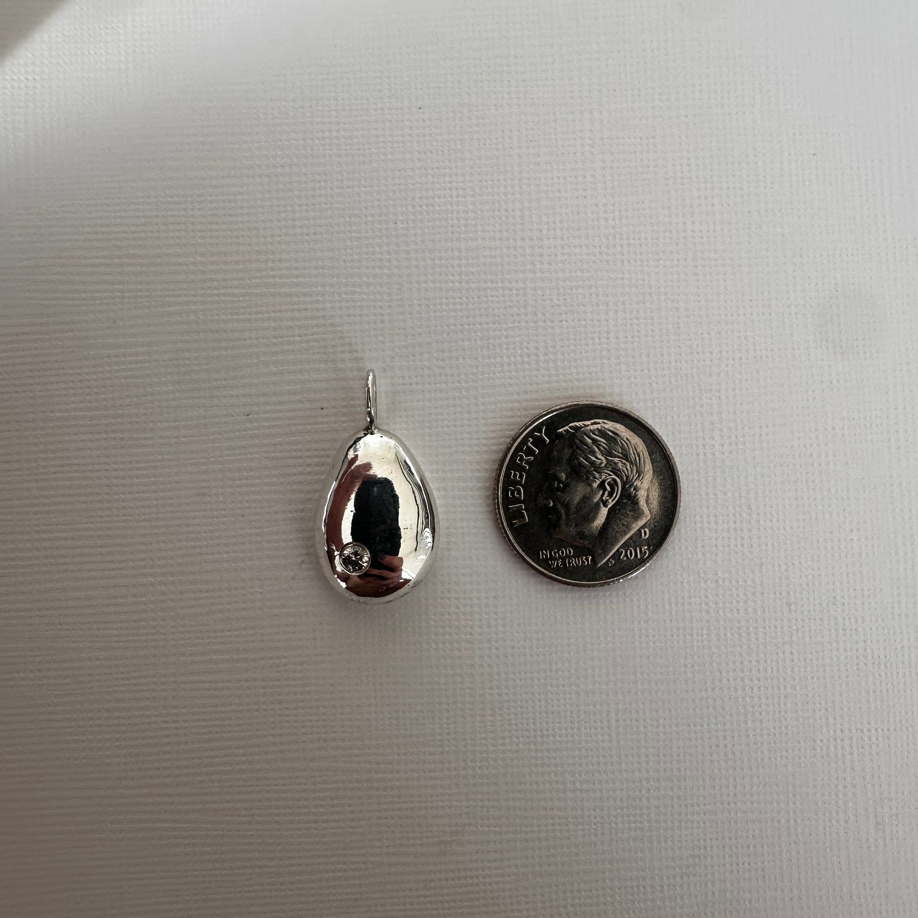 A small polished silver teardrop pendant with a reflective finish, shown next to a dime