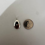 A small polished silver teardrop-shaped pendant or charm with a loop at the top, shown next to a U.S.