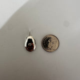 A small polished silver teardrop-shaped pendant or charm with a loop at the top, shown next to a U.S.