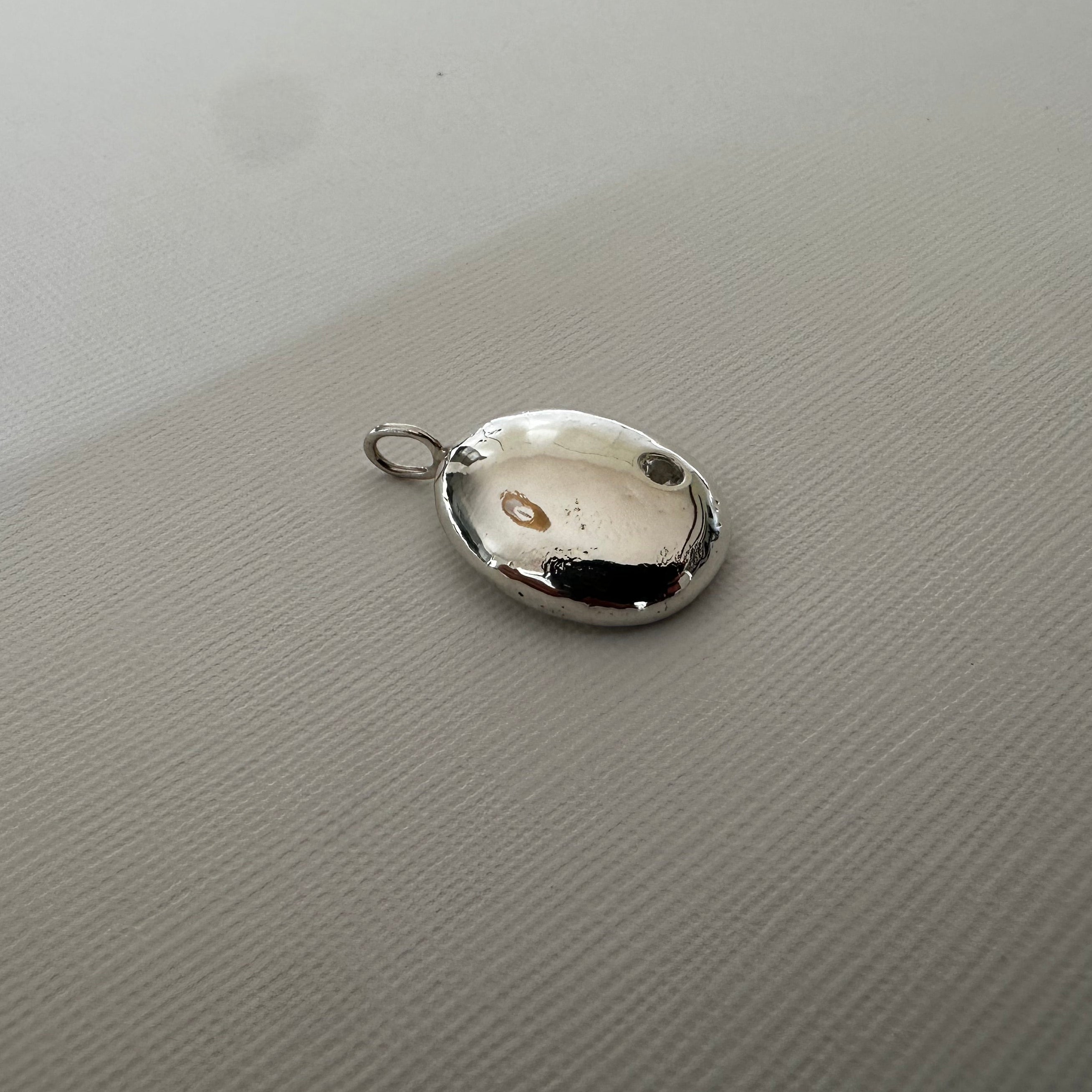 A polished silver oval pendant with a small attached loop, resting on a textured light gray surface.
