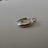 A polished silver oval pendant with a small hanging loop, resting on a textured white surface.