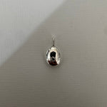A small polished silver teardrop-shaped pendant or charm with a reflective finish and a tiny loop at the top, shown on a light gray textured background.
