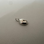 A small polished silver oval pendant with a loop at the top, resting on a textured light gray surface.