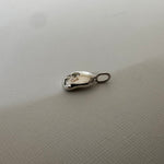 A small silver metal charm or pendant with a loop at one end, resting on a textured off-white surface.