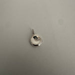 A small round silver pendant charm with a bail, photographed on a textured light gray surface.