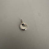 A small round silver pendant charm with a bail, photographed on a textured light gray surface.