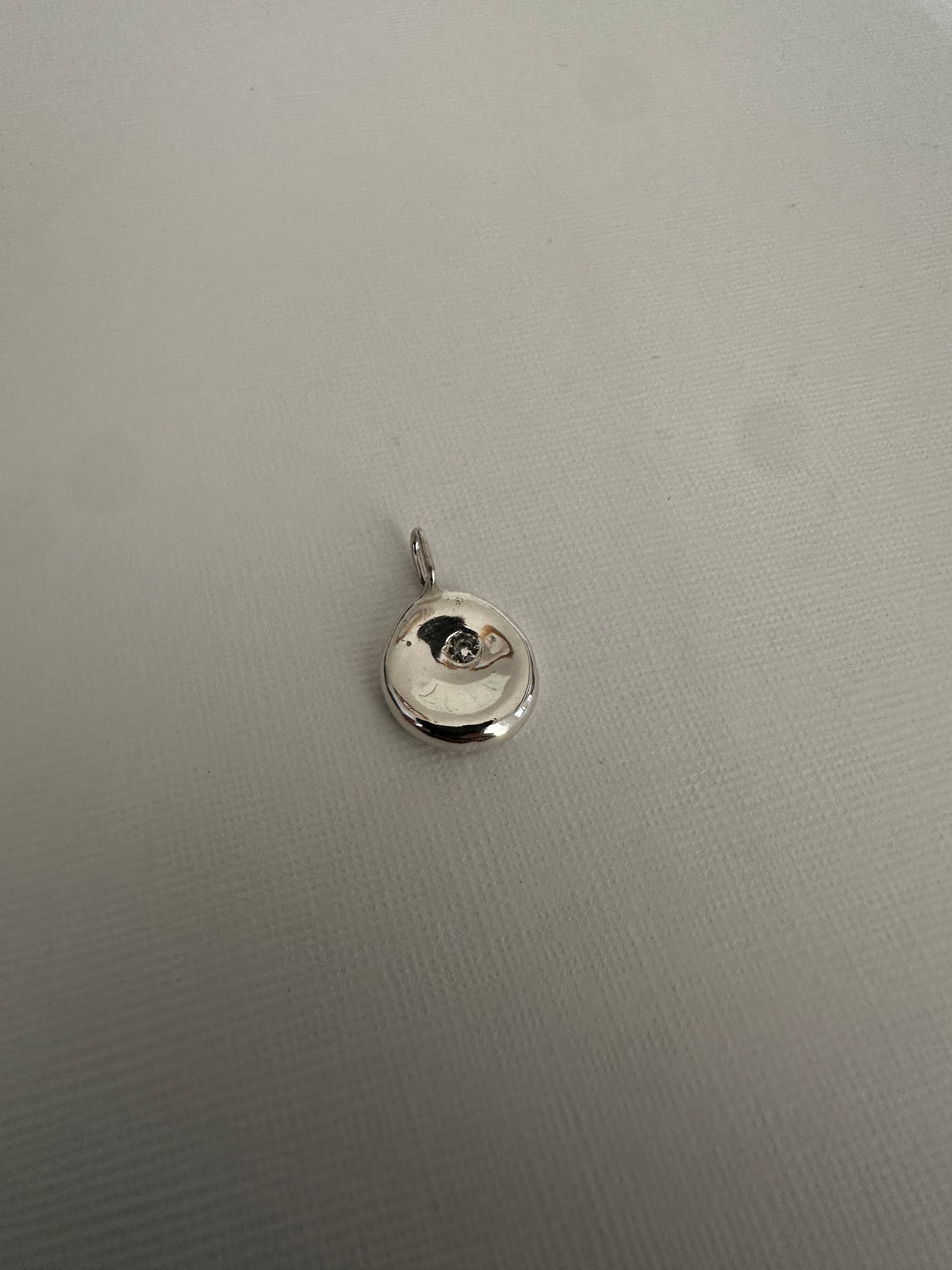 A small round silver pendant charm with a bail, photographed on a textured light gray surface.