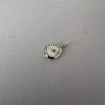 A small polished silver pendant or charm with a circular disc design and a tiny central dot, shown on a light gray textured background.