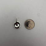 A small silver stud earring with a circular face and a thin post, shown on a light gray textured background with a US quarter coin above it for scale.