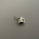 A small silver metallic charm shaped like a dog's head with a loop at the top, resting on a textured gray surface.