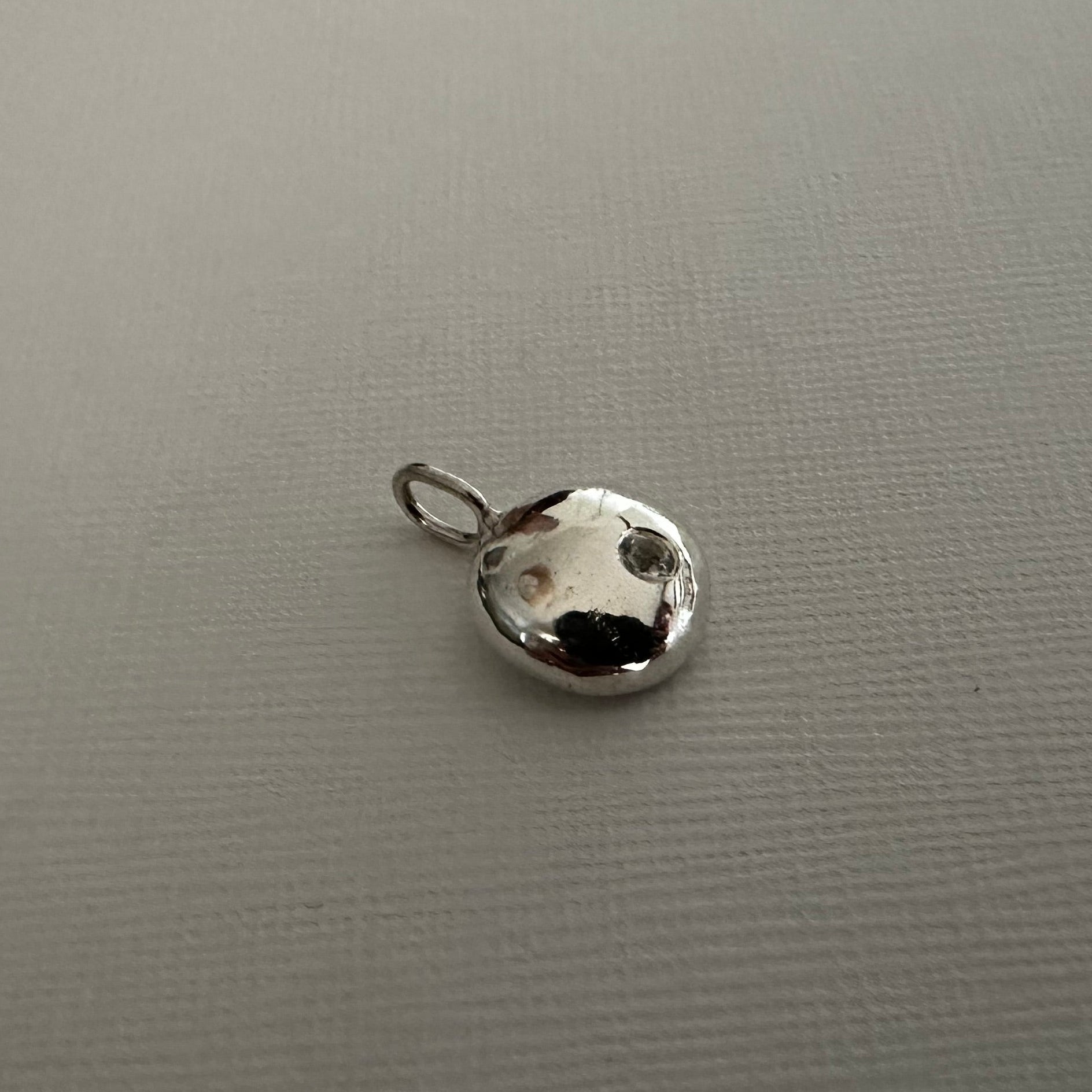 A small silver metallic charm shaped like a dog's head with a loop at the top, resting on a textured gray surface.