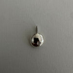 A small silver pendant charm with a polished dome and a tiny clear gemstone, shown on a textured gray background.