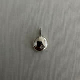 A small silver pendant charm with a polished dome and a tiny clear gemstone, shown on a textured gray background.