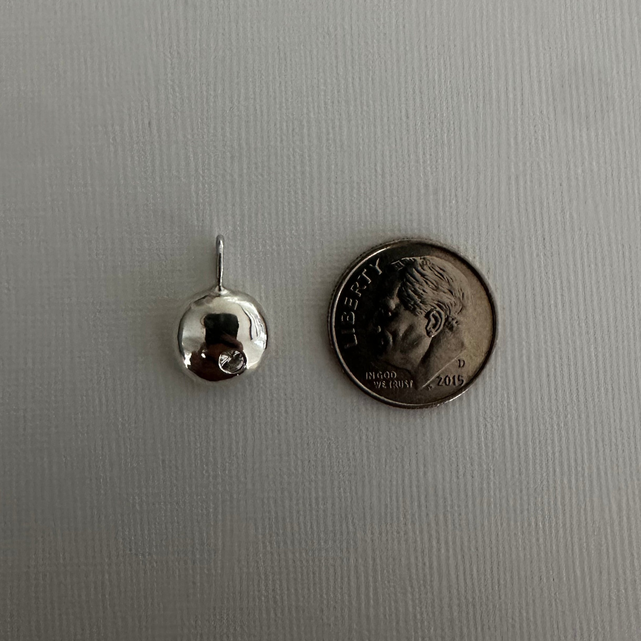 A small silver earring with a butterfly back is shown next to a US dime for scale, on a light gray textured background.