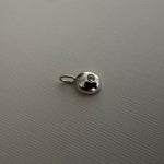 A small silver metallic charm with a loop at the top, photographed on a textured gray background.