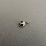 A small silver metal charm or pendant with a loop at the top, photographed on a textured light gray surface.