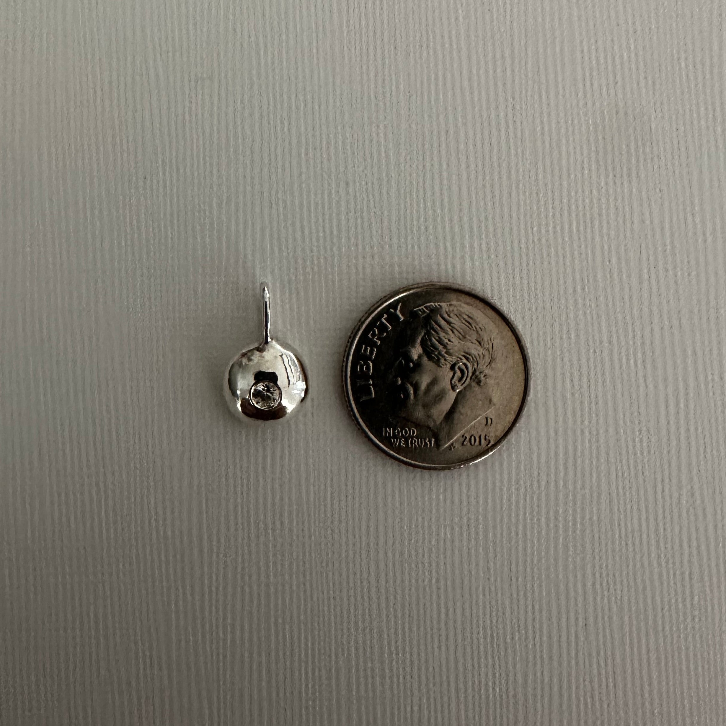 A small silver jewelry component, likely a bead or charm with a loop, shown next to a U.S.