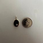 A small oval black pendant with a gold border and a tiny clear stone, shown next to a U.S.