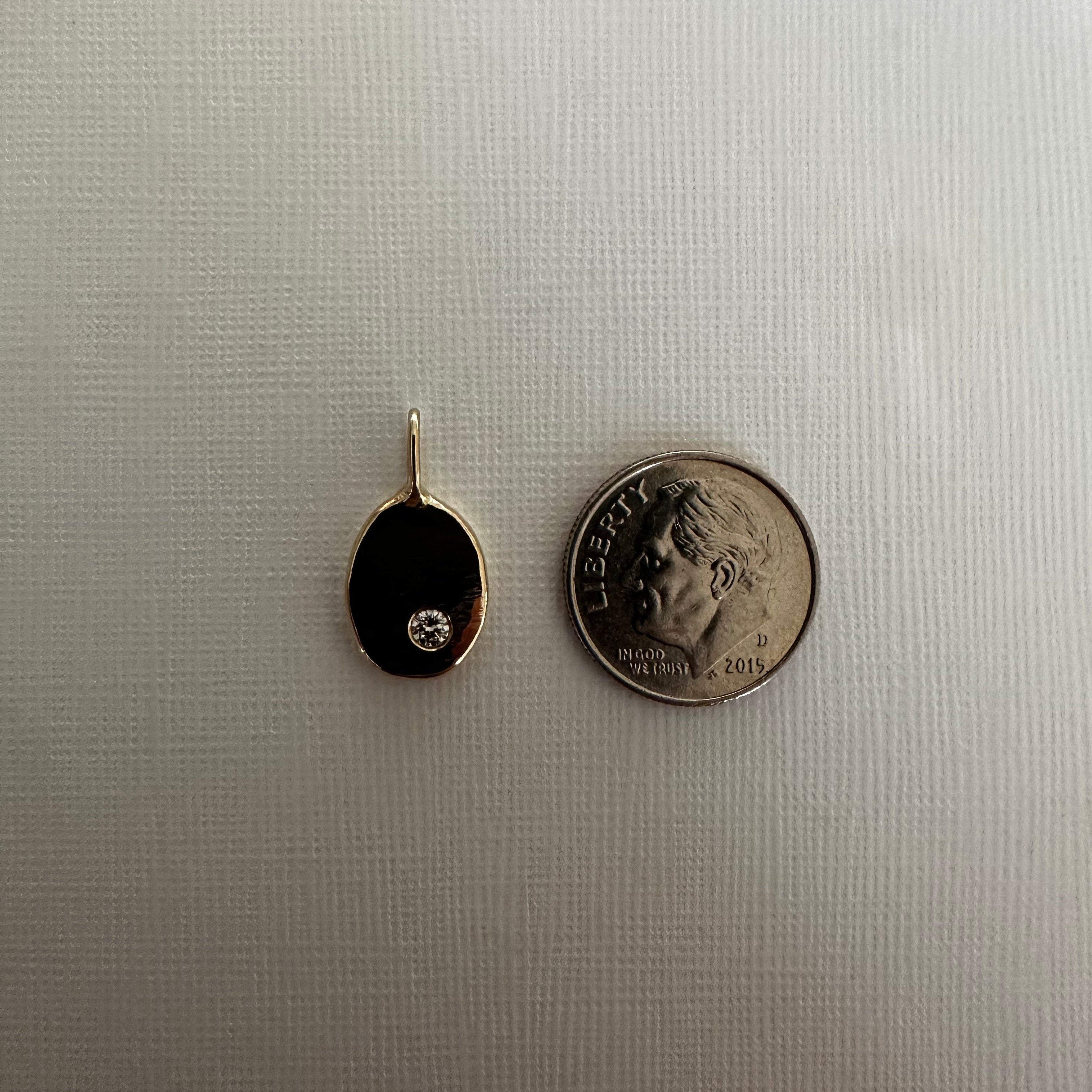 A small oval black pendant with a gold border and a tiny clear stone, shown next to a U.S.