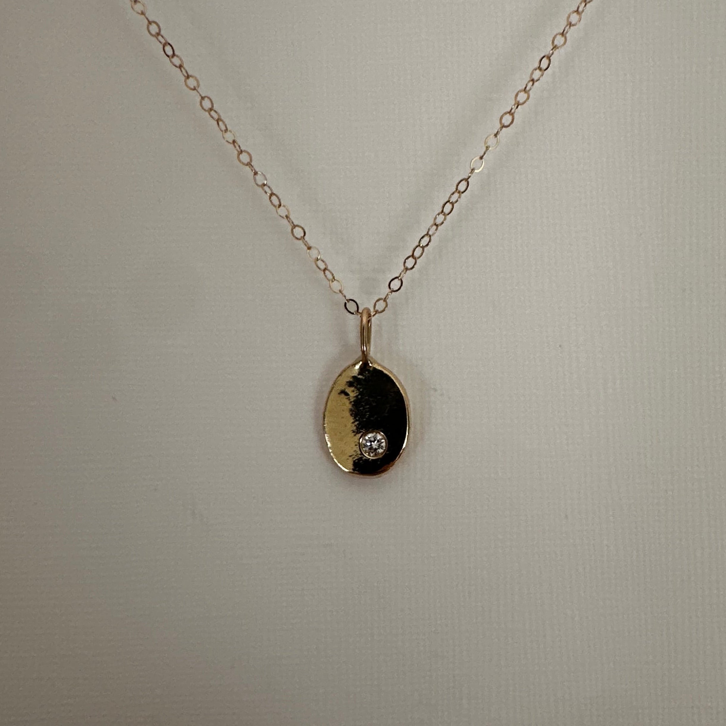 A delicate gold chain necklace with an oval pendant featuring a black and gold yin-yang symbol and a small clear gemstone, displayed against a light gray background.