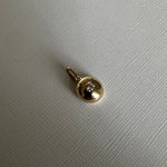 A small gold pendant with a round bezel-set clear gemstone, shown on a textured light gray surface.