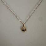 A delicate yellow gold chain necklace with a small spherical pendant containing a tiny clear gemstone, displayed against a light beige textured background.