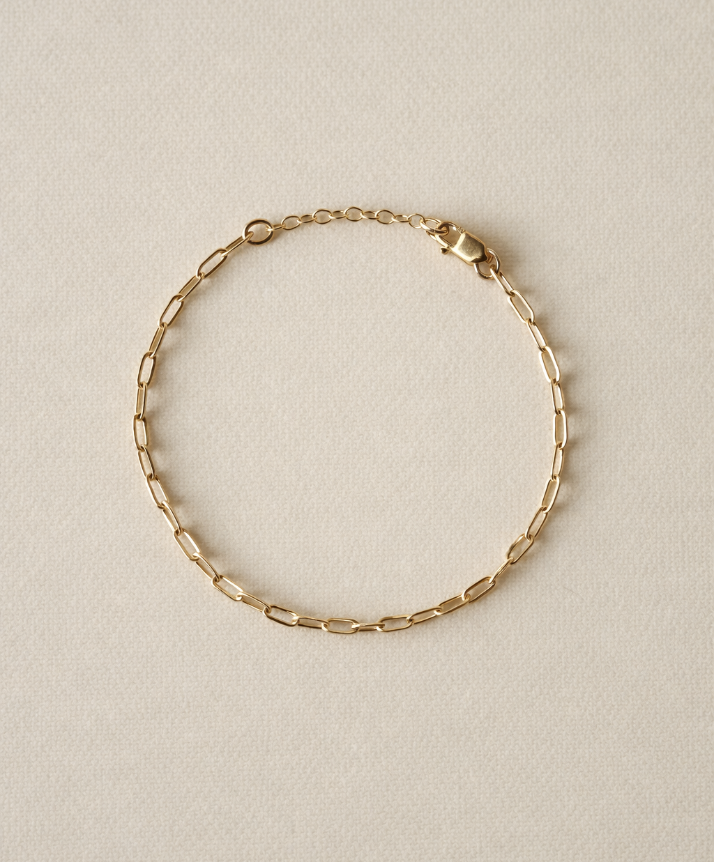 Paperclip gold fill chain bracelet on a beige background with one inch extender