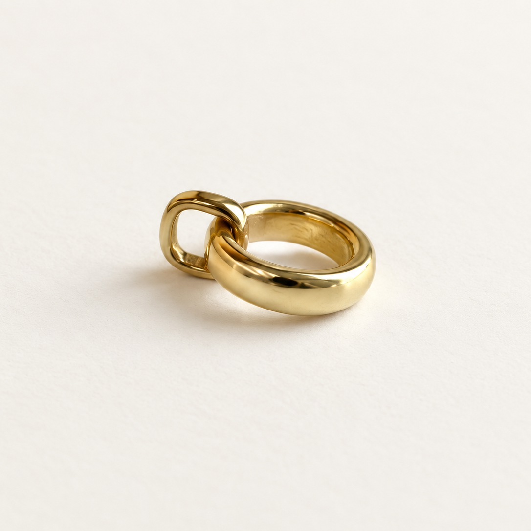 A polished gold pendant with a unique interlocking double-band design, photographed on a clean, light off-white background.