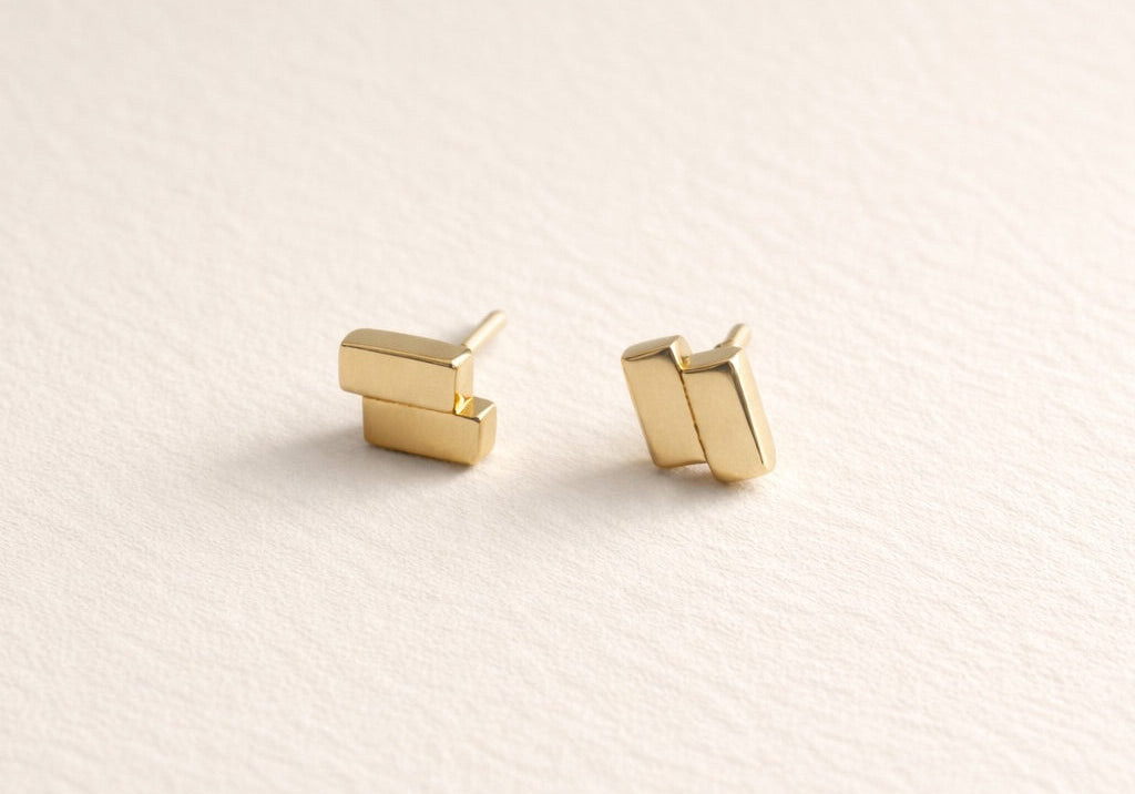 Pair of gold bar-shaped earrings on a light beige background