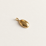 A small polished gold oval pendant with a loop at the top, photographed on a clean off-white textured background.