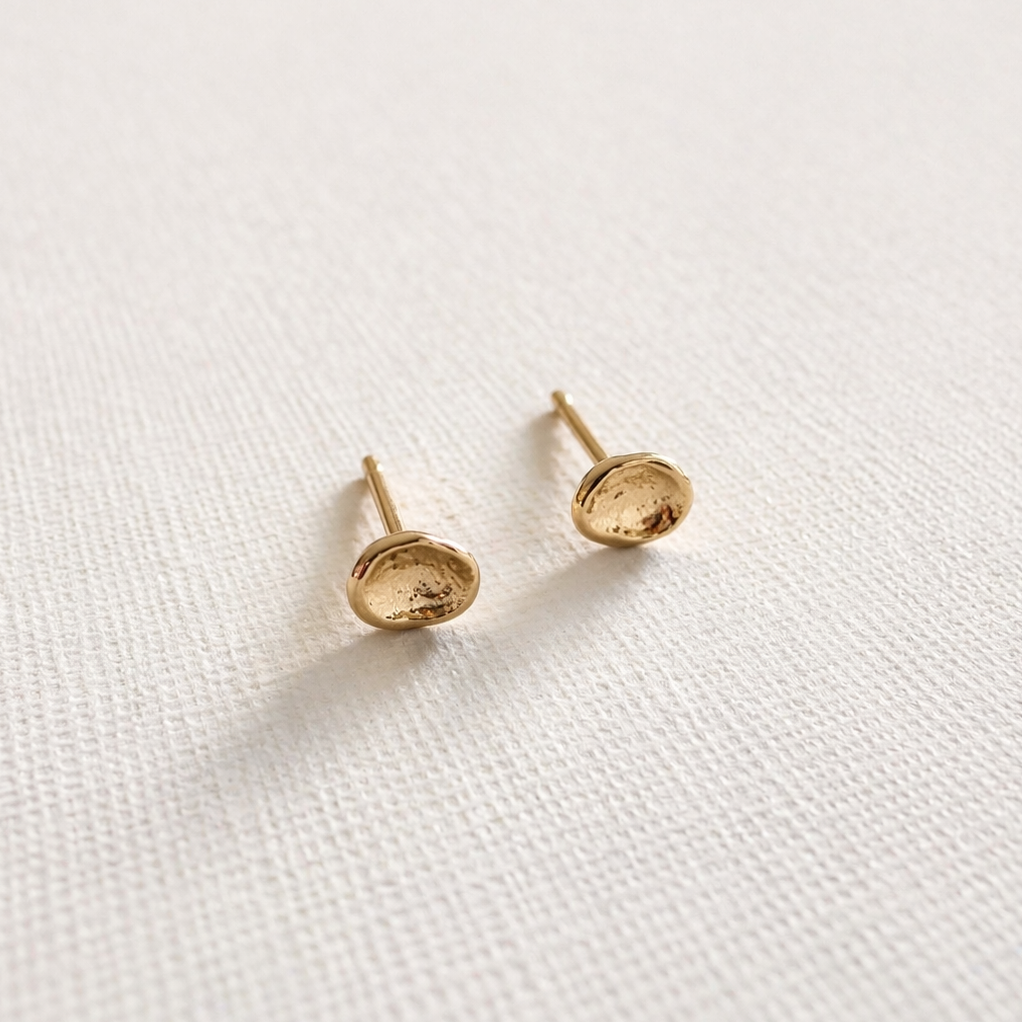 Pair of gold stud earrings on a white fabric background