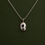 A silver chain necklace with a polished, organic-shaped silver pendant featuring a small clear gemstone, displayed against a dark green background.