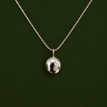 A silver chain necklace with a small, polished silver oval pendant featuring a black and white yin-yang symbol and a tiny clear gemstone, set against a dark green background.