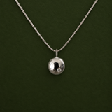 A silver chain necklace with a small, polished silver disc pendant, displayed against a solid dark green background.