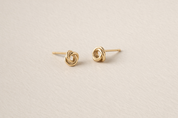 Pair of gold knot earrings on a beige background