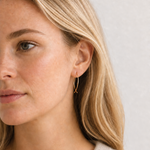 Close-up of a woman wearing gold hoop earrings against a neutral background