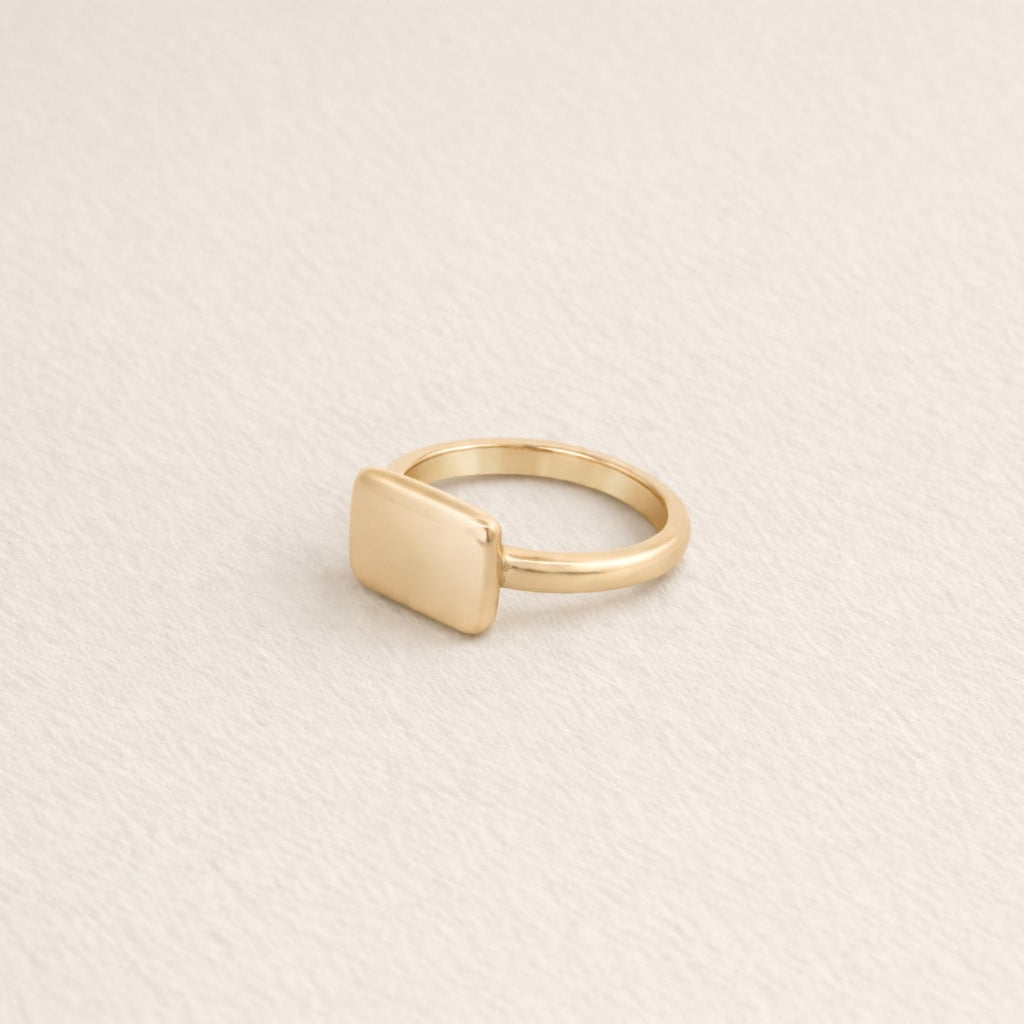 Gold rectangle signet ring on a beige background