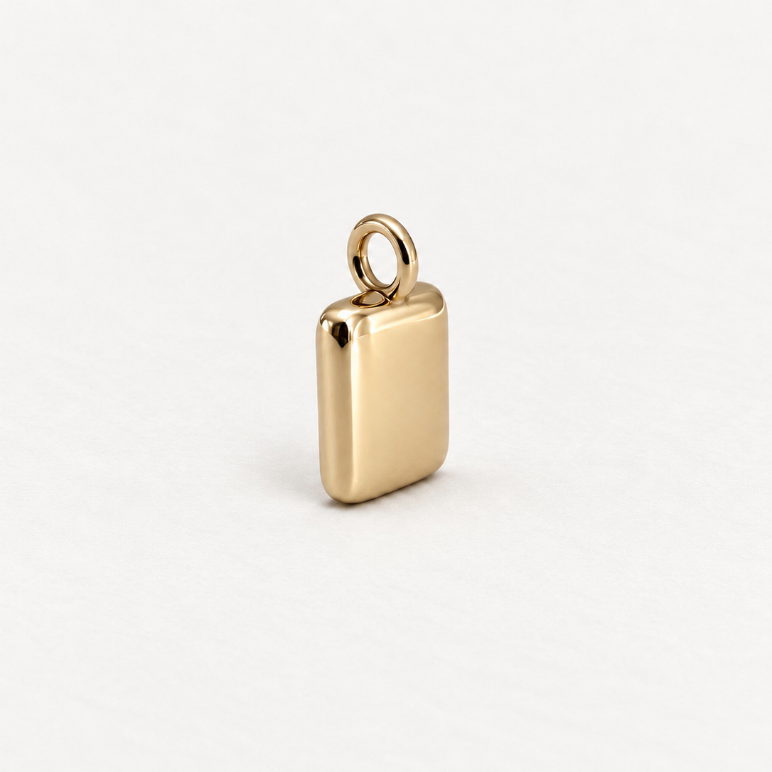 A small polished gold rectangular pendant with rounded corners and a top loop, photographed on a clean white background.