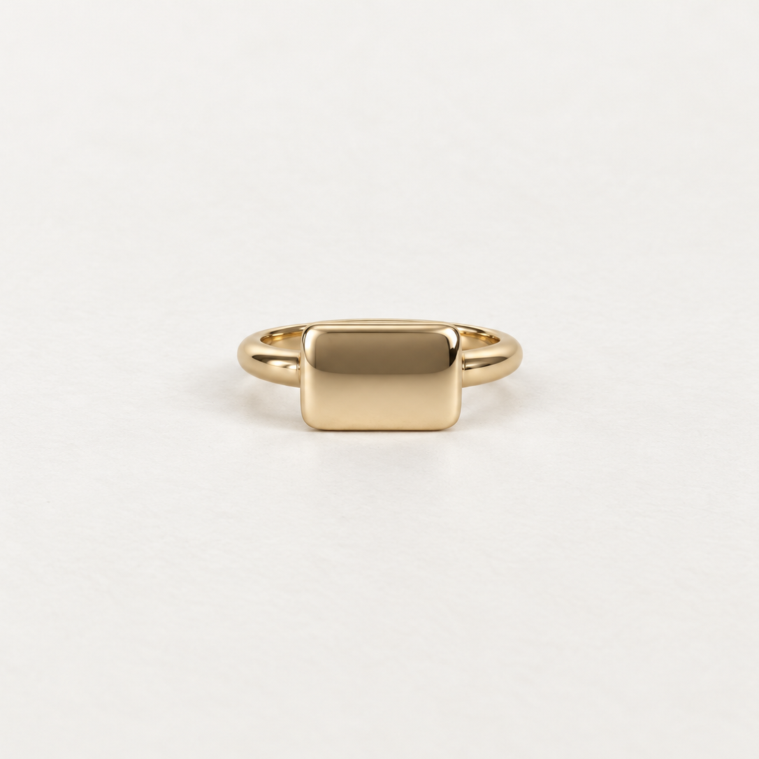 A minimalist gold signet ring with a flat, polished rectangular face, shown on a clean white background.